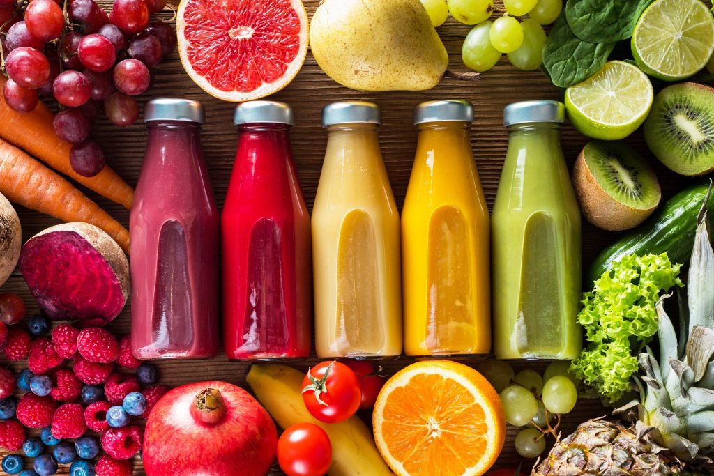 Colorful juices in bottles surrounded by fruit